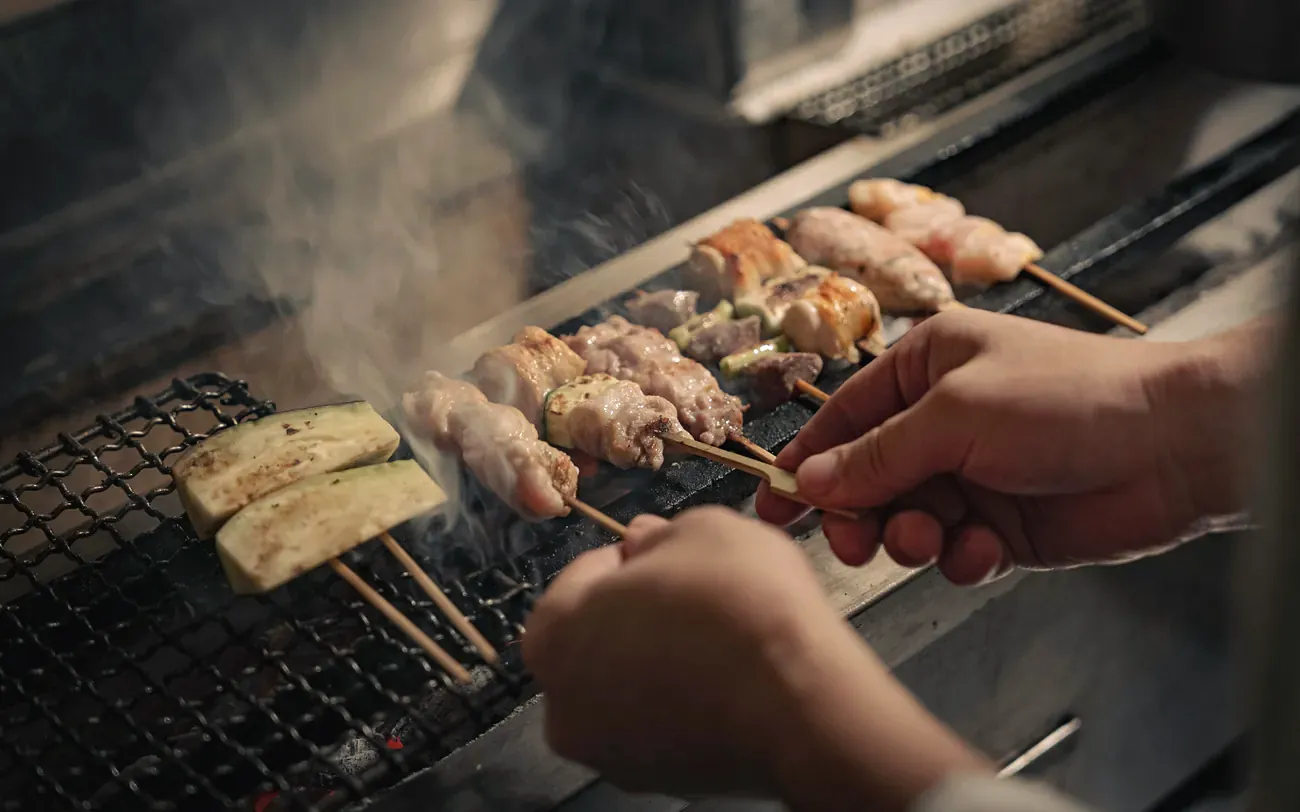 Yakitori Suzune의 그릴에서 꼬치를 뒤집는 손